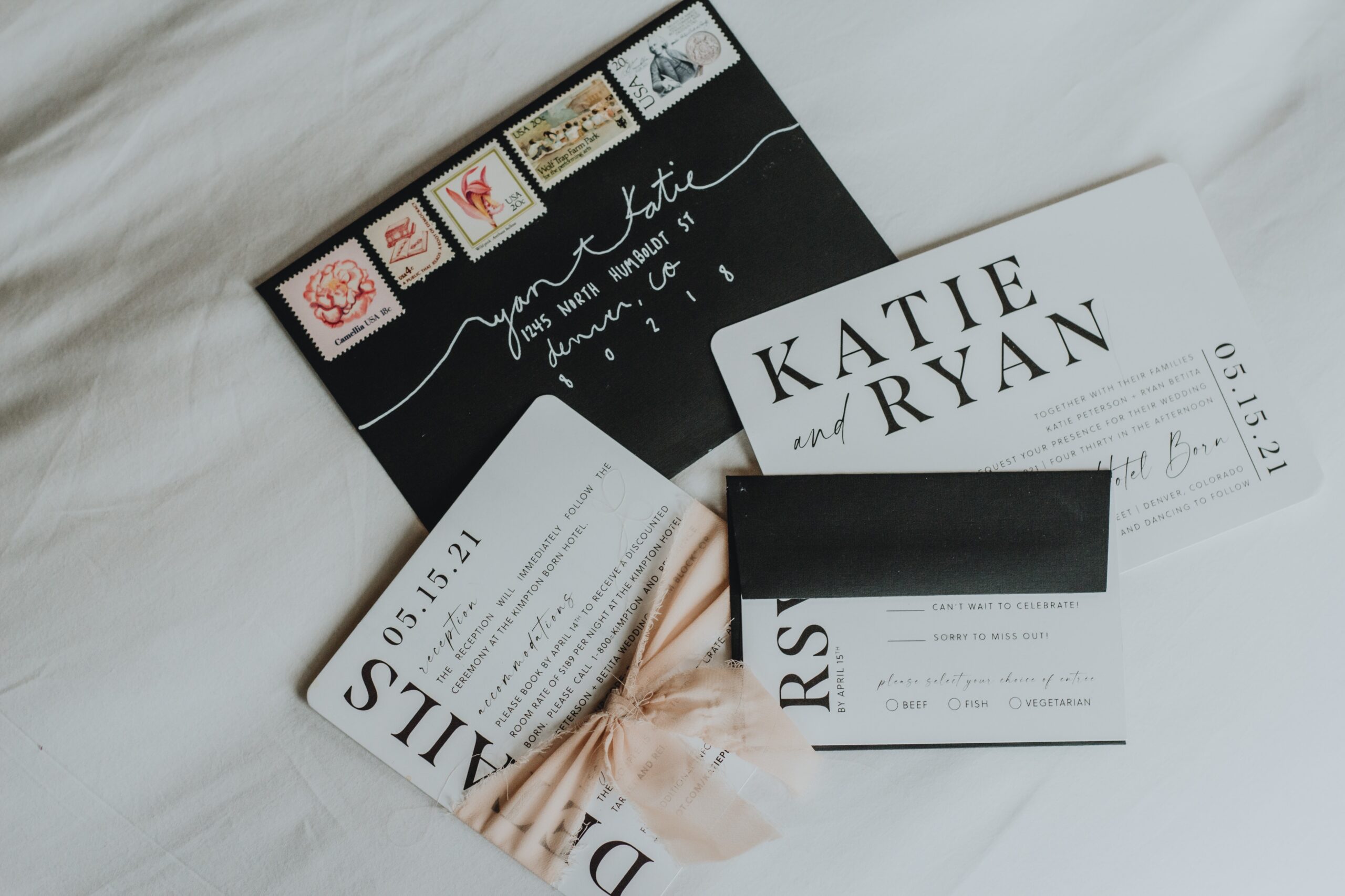 black and white wedding invite spread on a table with a pink bow around it.