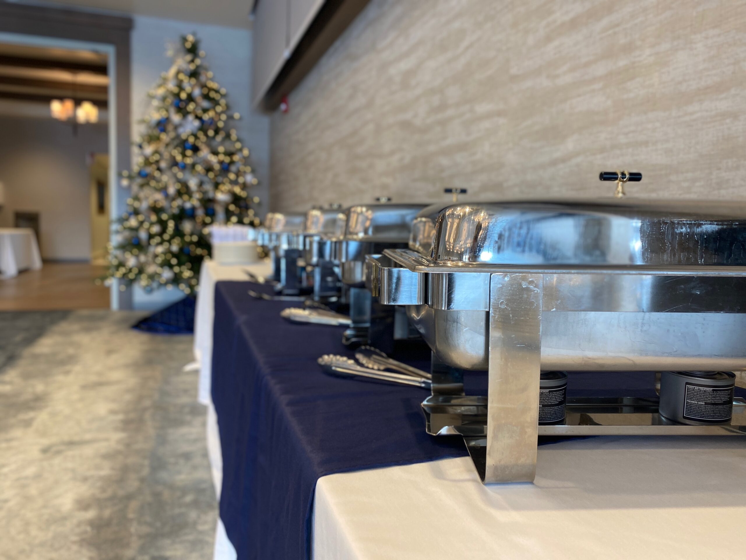 buffet with hot food in closed silved containers with a christmas tree in the end of the table