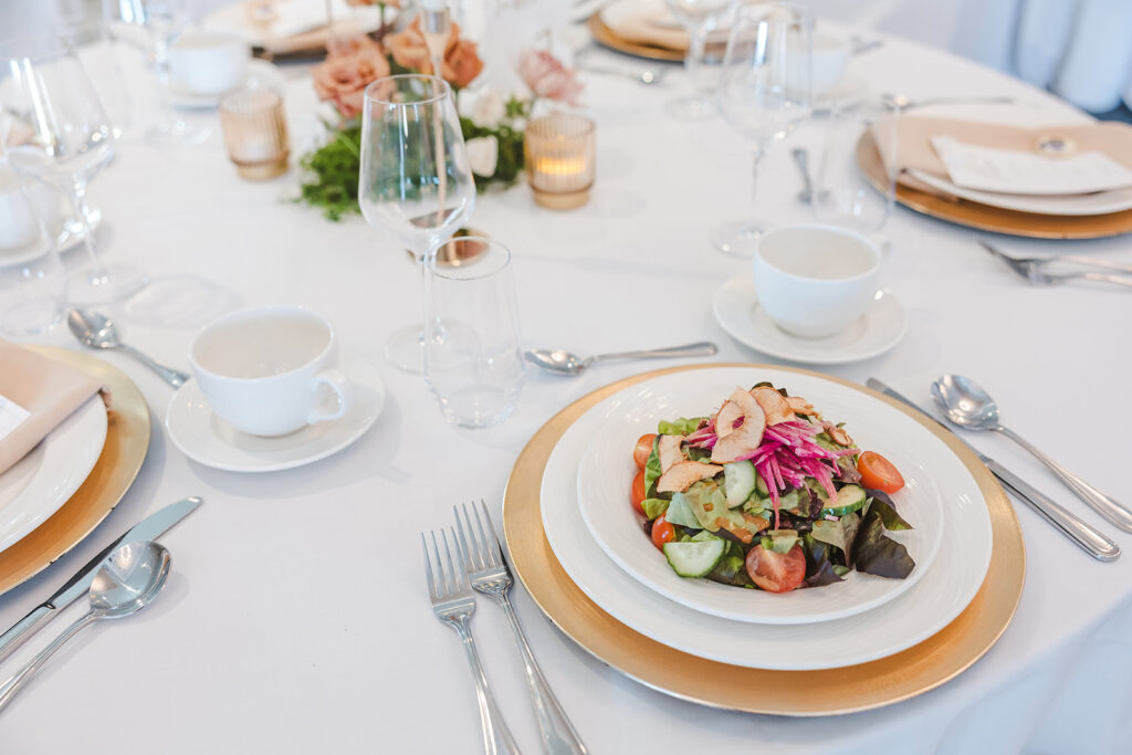 Formal table setting with salad course, gold charger, and white dinnerware