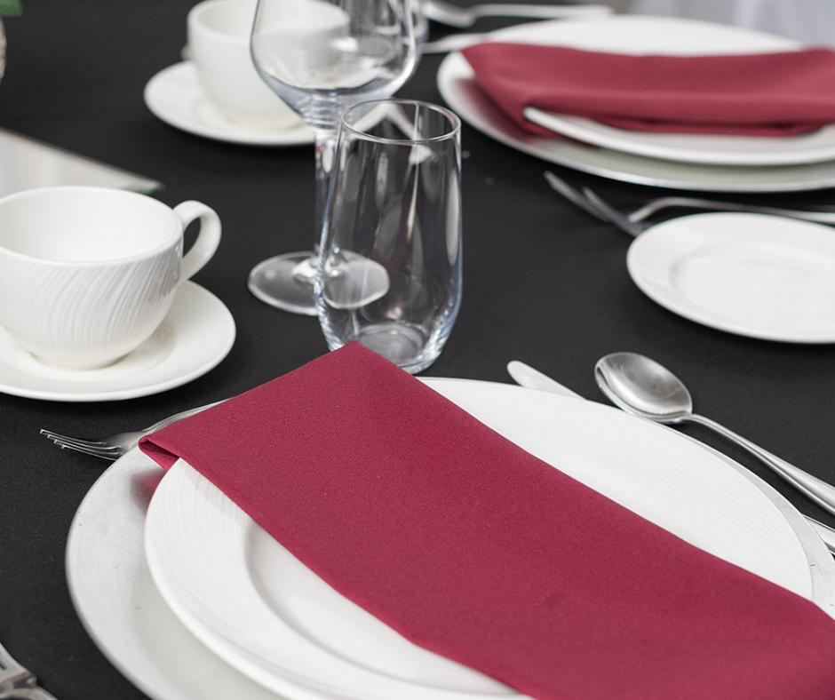 Formal table setting with white plates, glassware, and a folded burgundy napkin